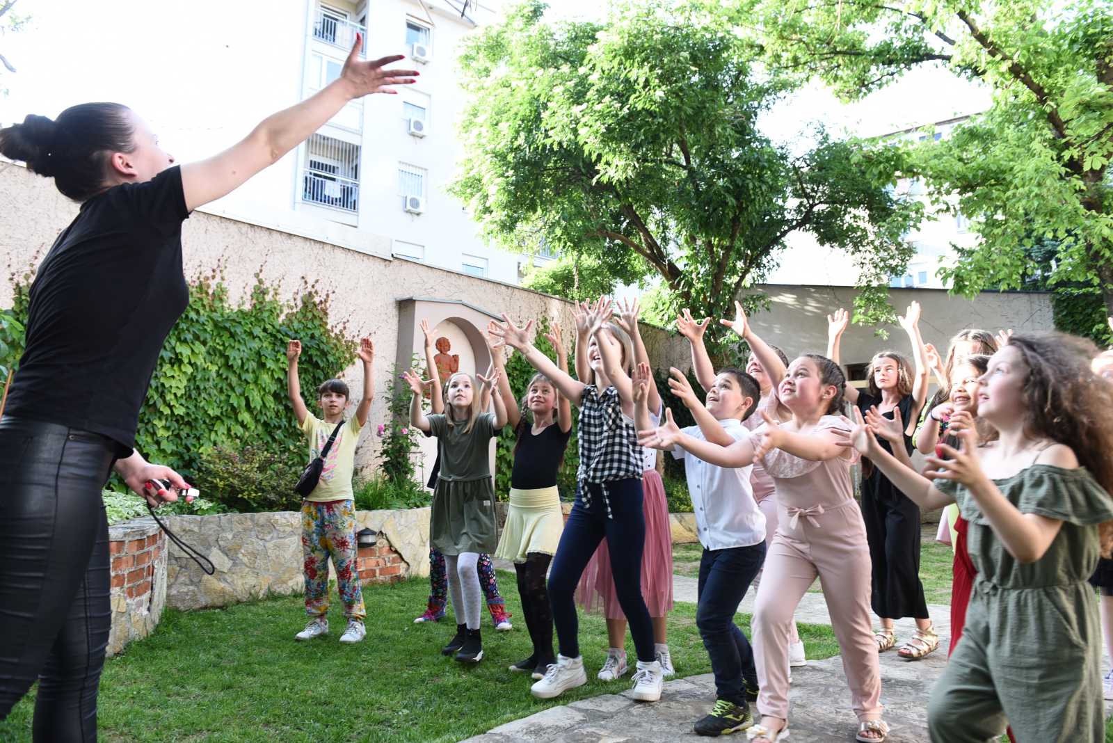 Učiteljica razbacuje konfete iznad dece koja ih radosno dočekuju s rukama u visu